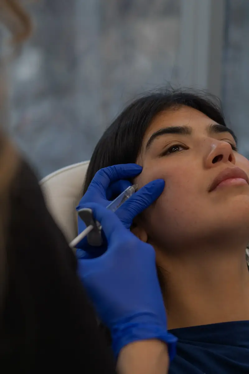 A clinician in blue gloves treating a patient's face at the clinic