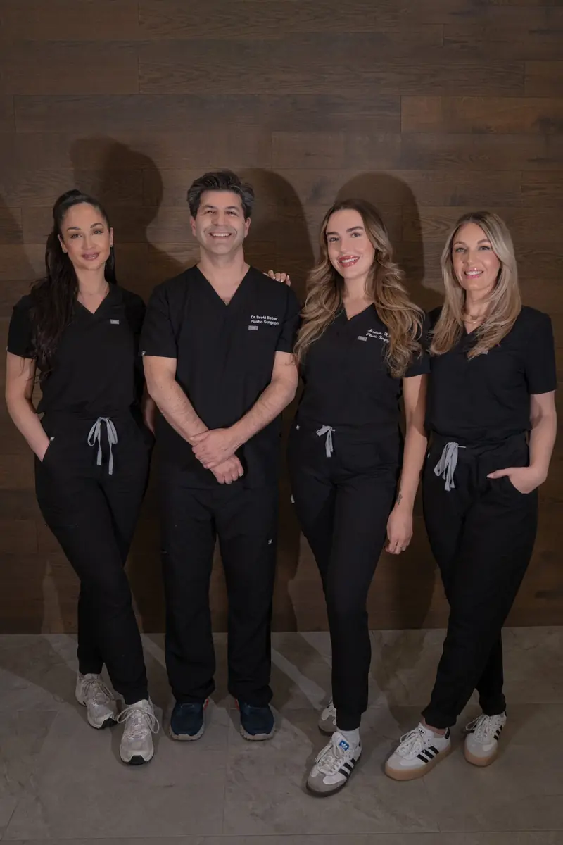 Dr. Beber's team standing together against a walnut wall